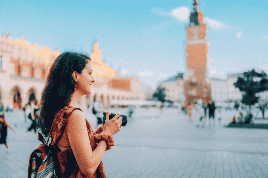 Mulher viajante segurando uma câmera em uma praça histórica na Europa, durante viagem solo.