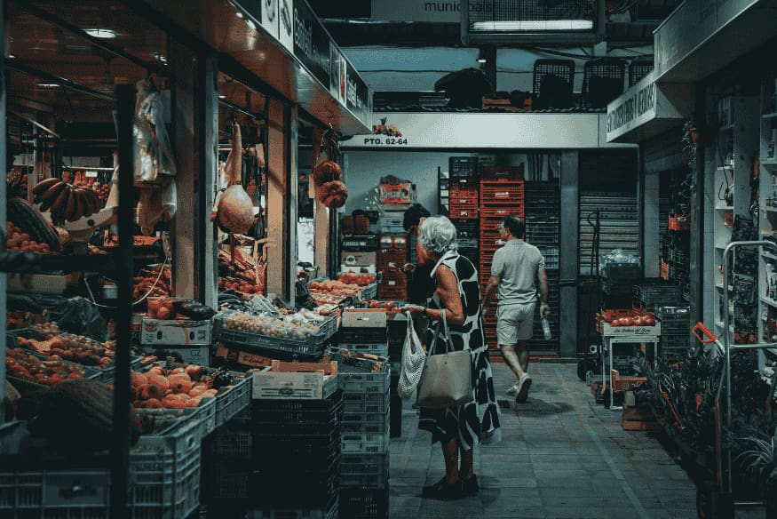 Turista comprando frutas e legumes em mercado municipal, apoiando o comércio local como forma de turismo sustentável nas grandes cidades.