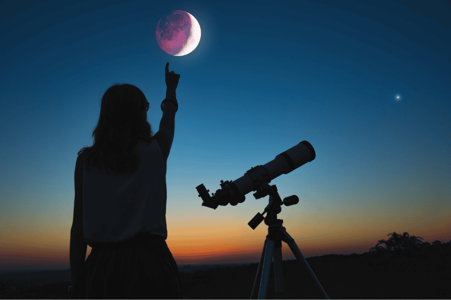 Silhueta de observadora apontando para a Lua ao lado de um telescópio ao entardecer, ilustrando como astrônomos medem distâncias no espaço.