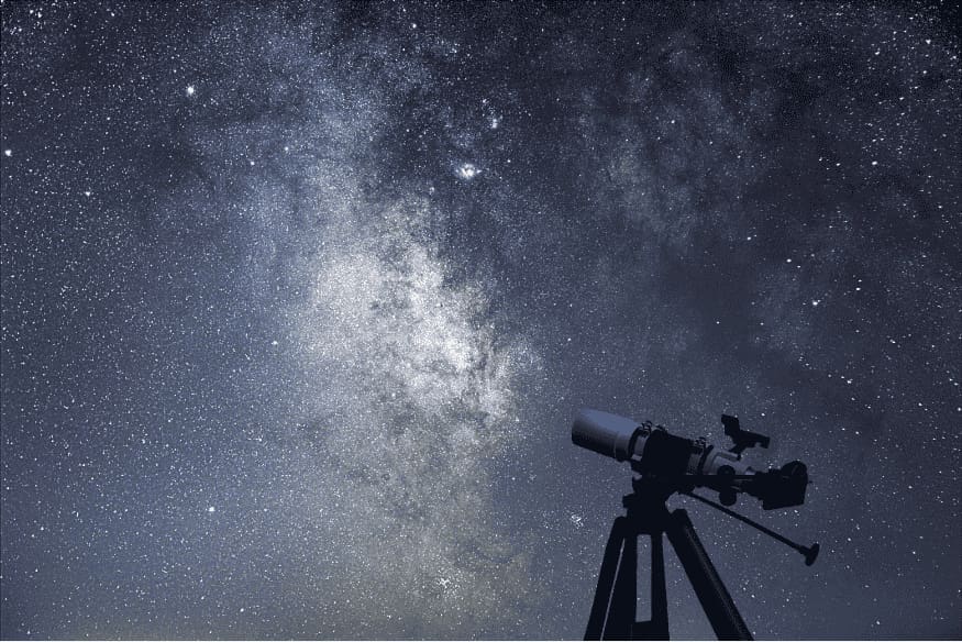 Céu estrelado com a Via Láctea e telescópio em tripé, cenário típico para astrofotografia de longa exposição.