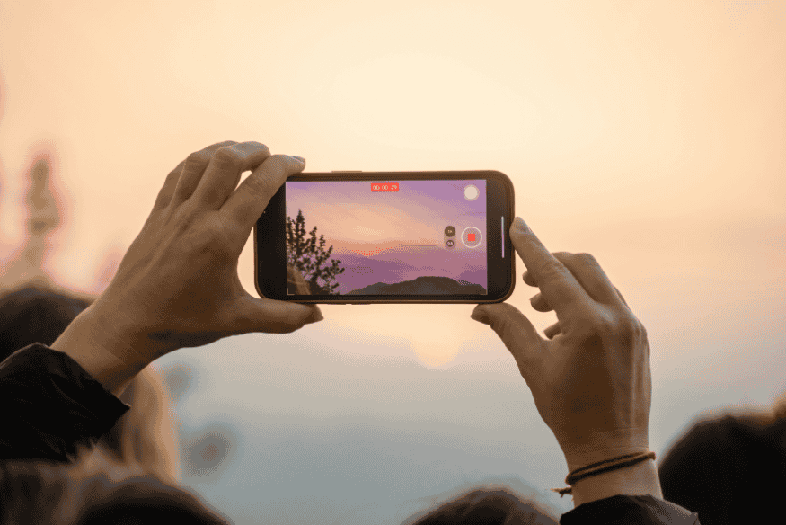 Pessoa registrando o céu e a paisagem com smartphone, exemplo de uso do celular para fotografar cenas ao entardecer e à noite.