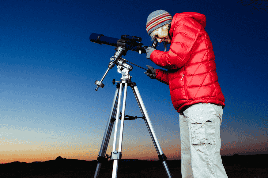 Observador usando telescópio em tripé ao ar livre, em cena de campo para estudar e registrar eclipses.