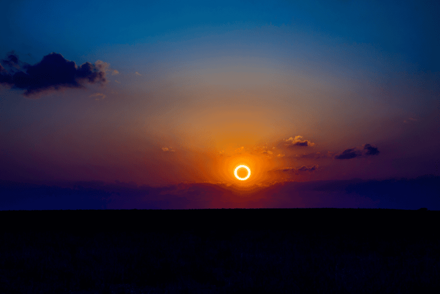 Eclipse solar anular no horizonte com “anel de fogo” brilhante em céu colorido ao entardecer.