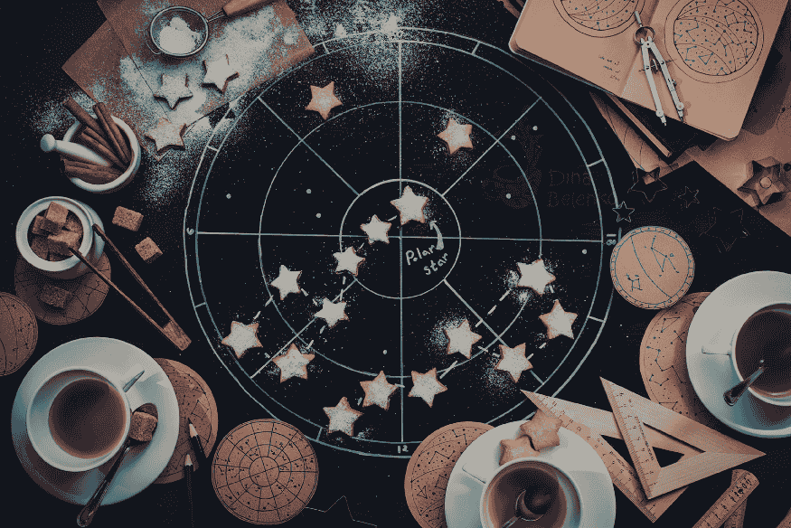 Mesa com mapa astral e símbolos de astrologia, com estrelas sobre um círculo do zodíaco, ilustrando crenças sobre eclipses.