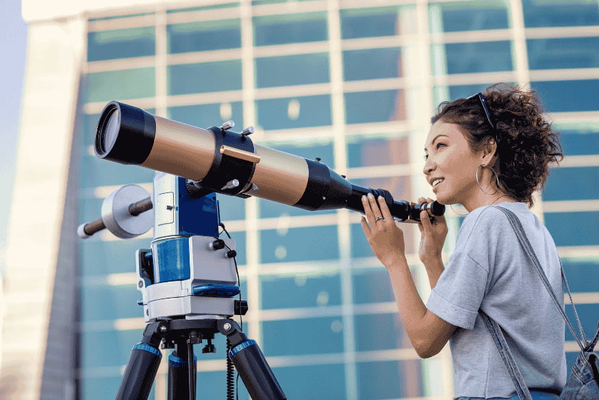 Pessoa observando por telescópio em ambiente urbano, representando a escolha do primeiro telescópio para iniciantes na astronomia.
