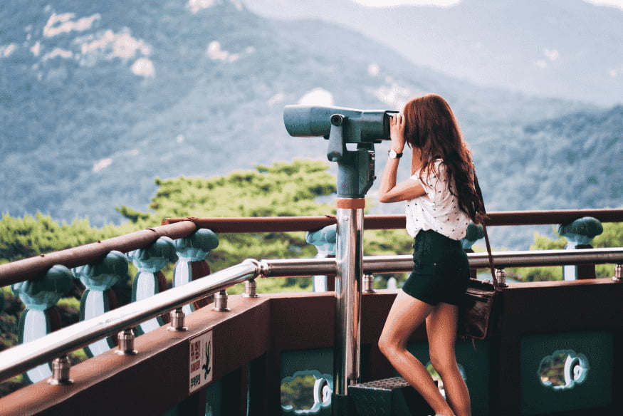 Pessoa usando luneta em mirante com vista para montanhas, exemplo de atividade comum em eventos de observação astronômica.