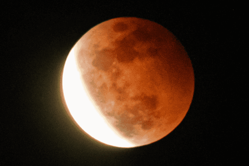 Lua com coloração avermelhada e parte clara visível, mostrando transição de um eclipse lunar e o efeito da sombra da Terra.