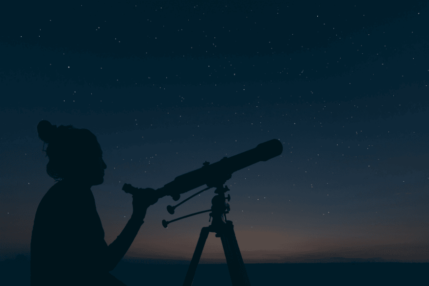 Pessoa observando o céu com telescópio ao entardecer, atividade útil para reconhecer estrelas e constelações visíveis à noite.