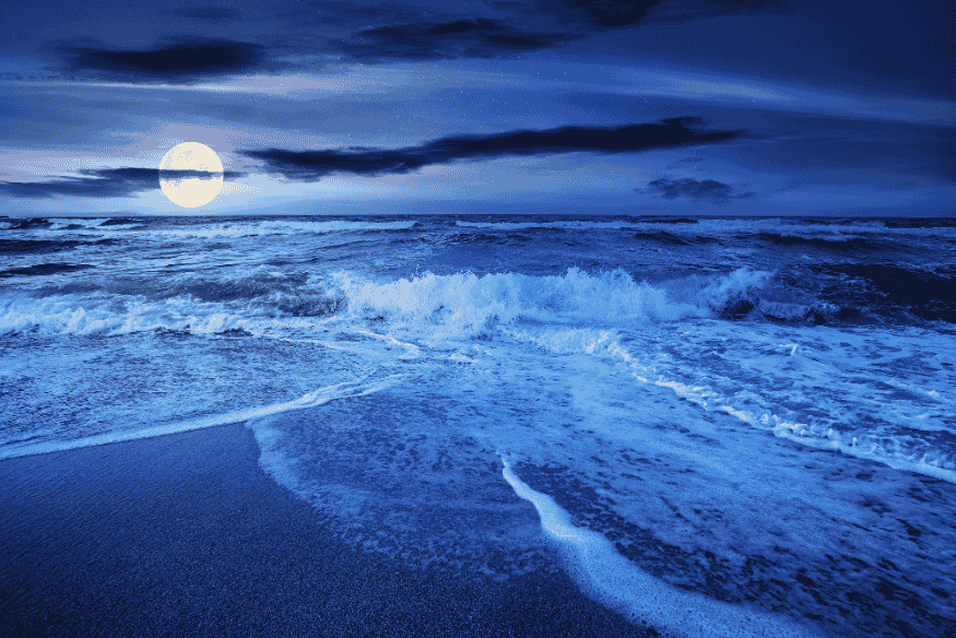 Oceano com ondas e Lua no horizonte ao entardecer, cenário associado a marés mais altas em períodos de perigeu.