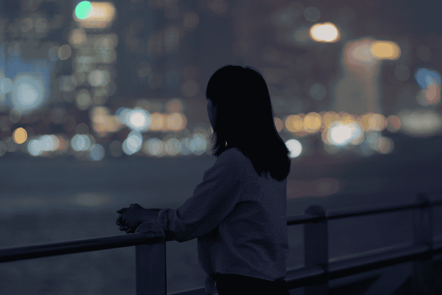 Pessoa observando a cidade à noite com luzes desfocadas ao fundo, cenário que representa os desafios da observação do céu em áreas urbanas.