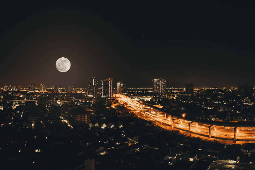 Lua cheia sobre a cidade iluminada à noite, exemplo de astro visível mesmo com poluição luminosa em centros urbanos.