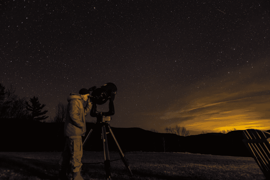 Pessoa observando o céu noturno com telescópio em tripé, exemplo de equipamento usado para localizar cometas com mais detalhes.