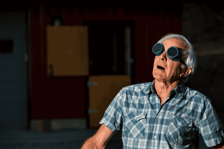 Homem usando óculos de proteção para eclipse solar e olhando para o céu, exemplo de observação segura do Sol.