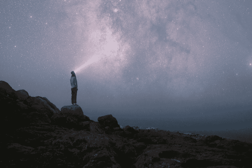 Pessoa observando o céu noturno em área aberta, prática comum para identificar planetas visíveis a olho nu longe da poluição luminosa.